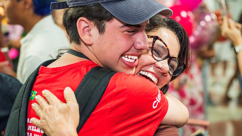 Jovem de boné e uma mulher de óculos se abraçando, emocionados, no evento da Happy Tour