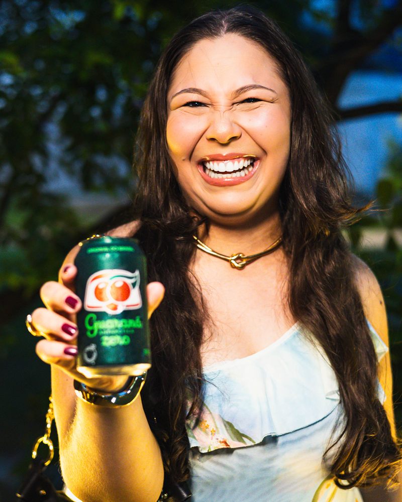 Convidada rindo e mostrando uma lata de Guaraná no evento da Ambev